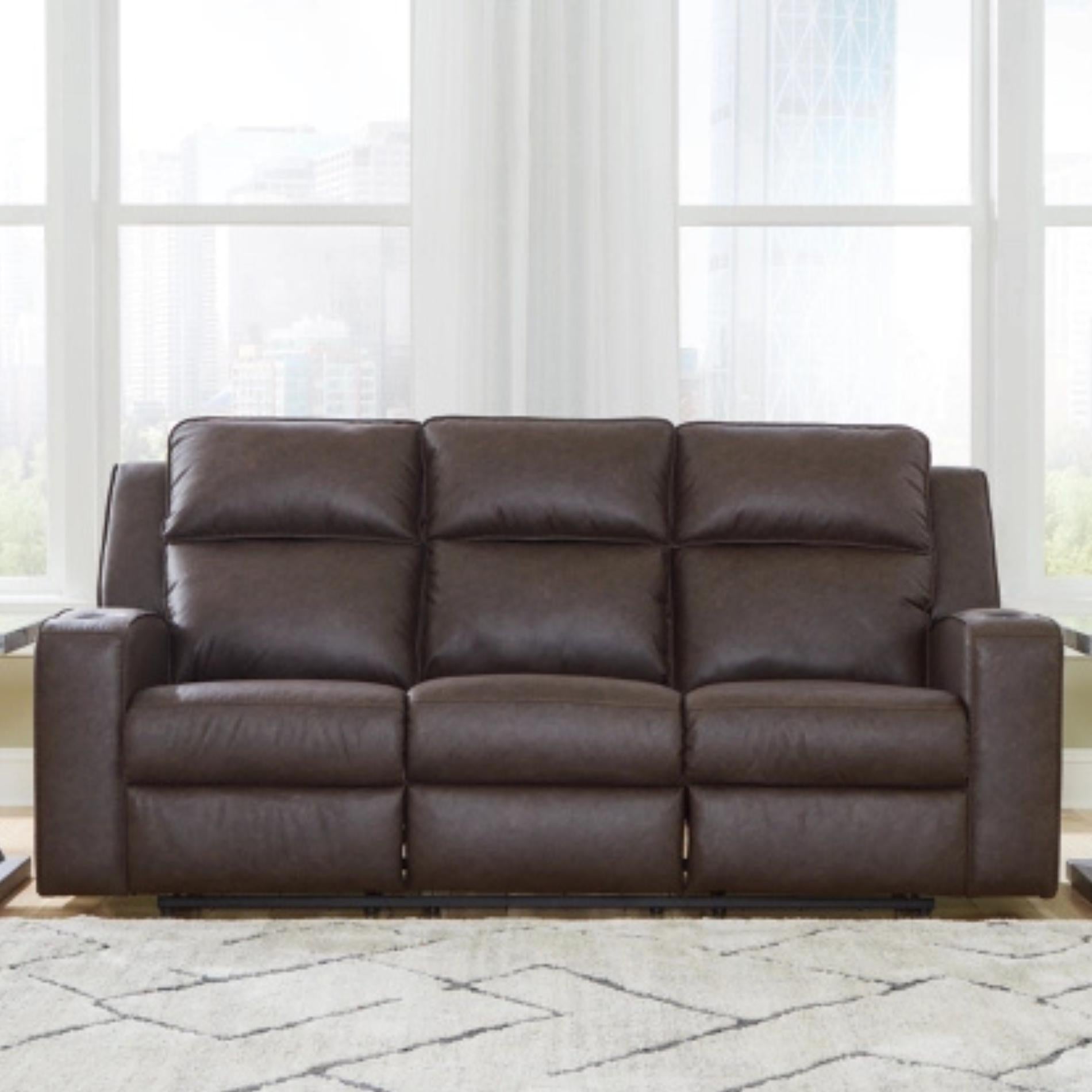 Brown leather sofa in a room with large windows and light-colored carpet.