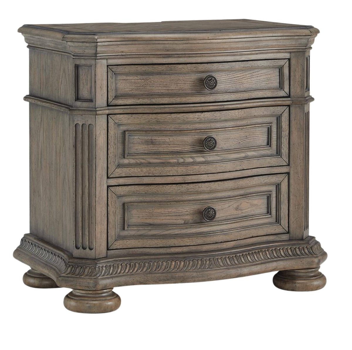 A three-drawer nightstand with a distressed gray-brown wood finish, featuring round dark metal knobs and decorative carved details on the front and base, set against a plain white background.