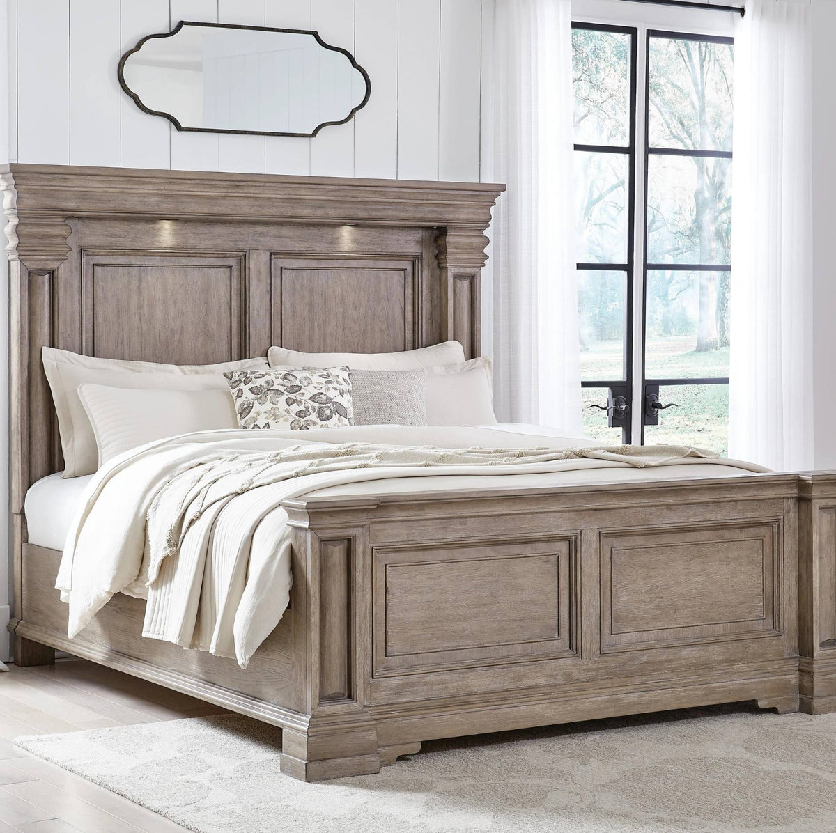 A rustic gray-brown wooden bed frame with a tall paneled headboard and matching footboard, styled with white bedding and pillows in a bright bedroom setting.