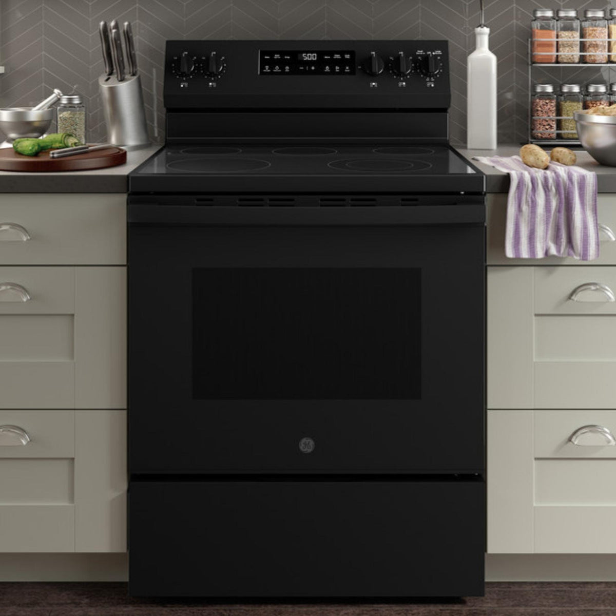 Black electric stove in a kitchen setting with gray cabinets and various kitchen items.
