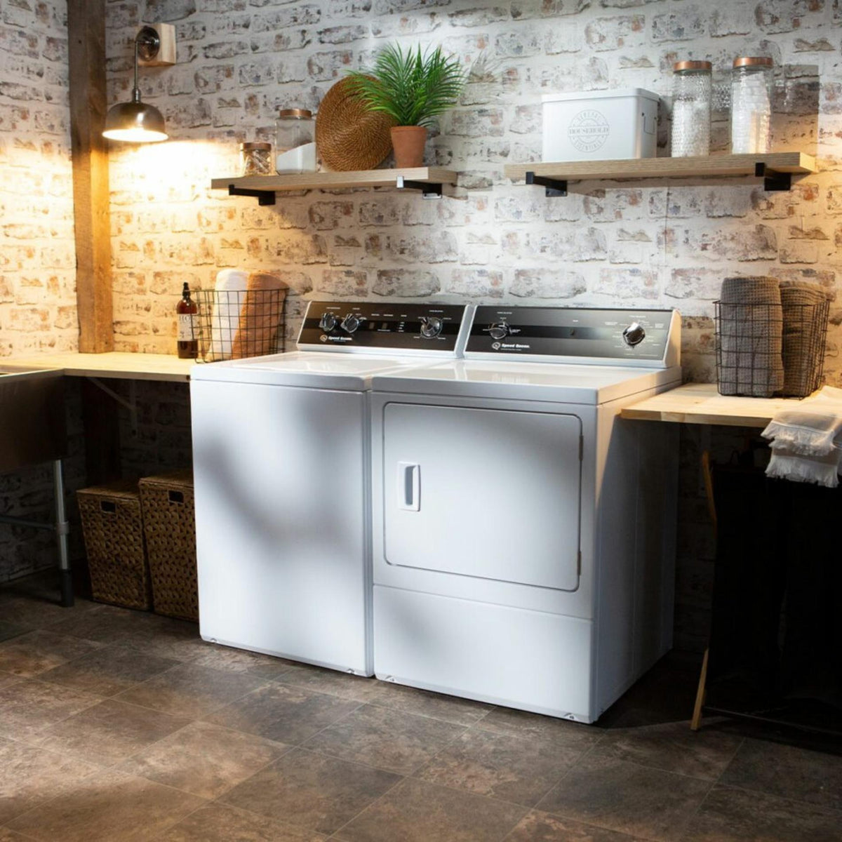 White laundry machine and dryer in a room with brick walls and wooden shelves.