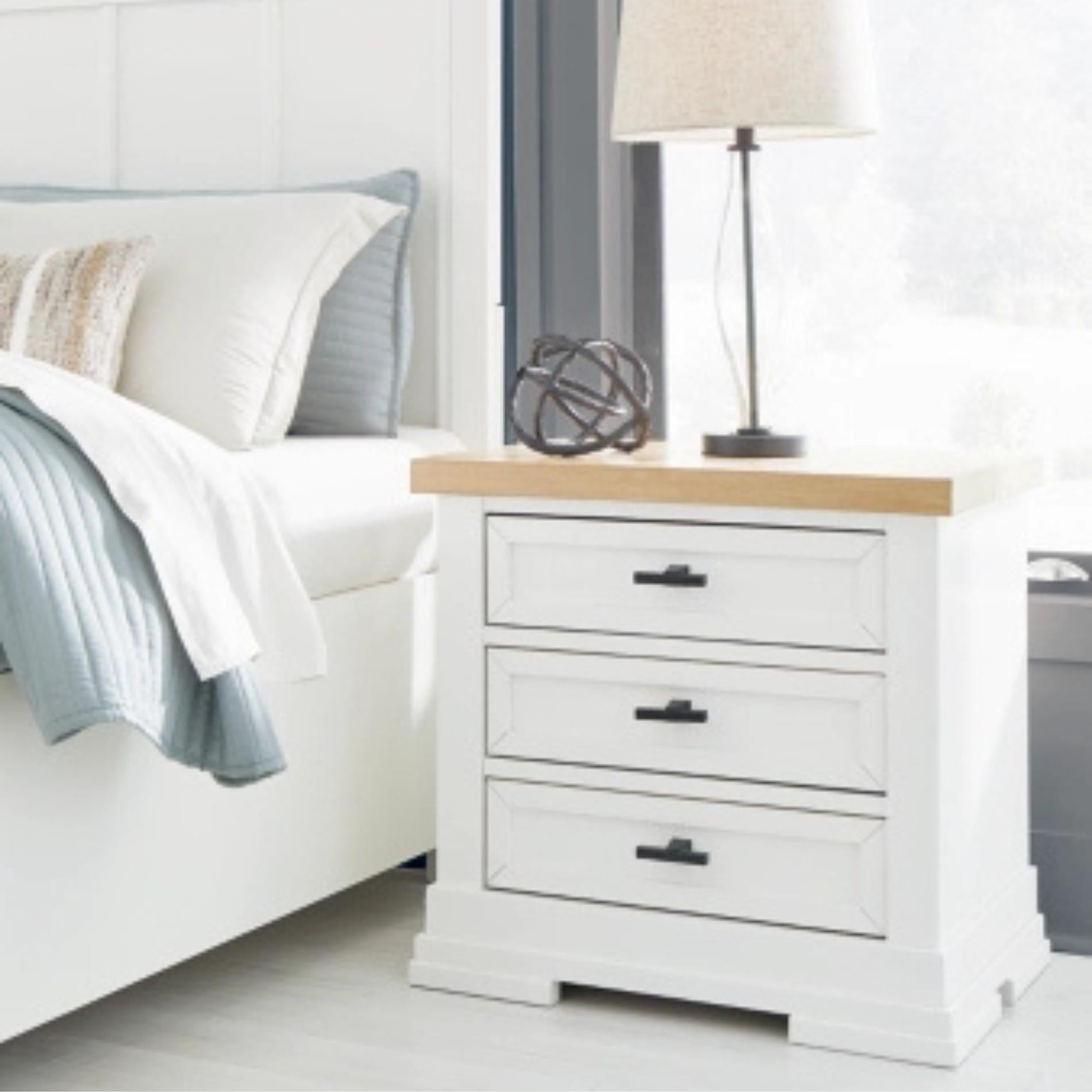 White nightstand with wooden top next to a bed in a bedroom setting