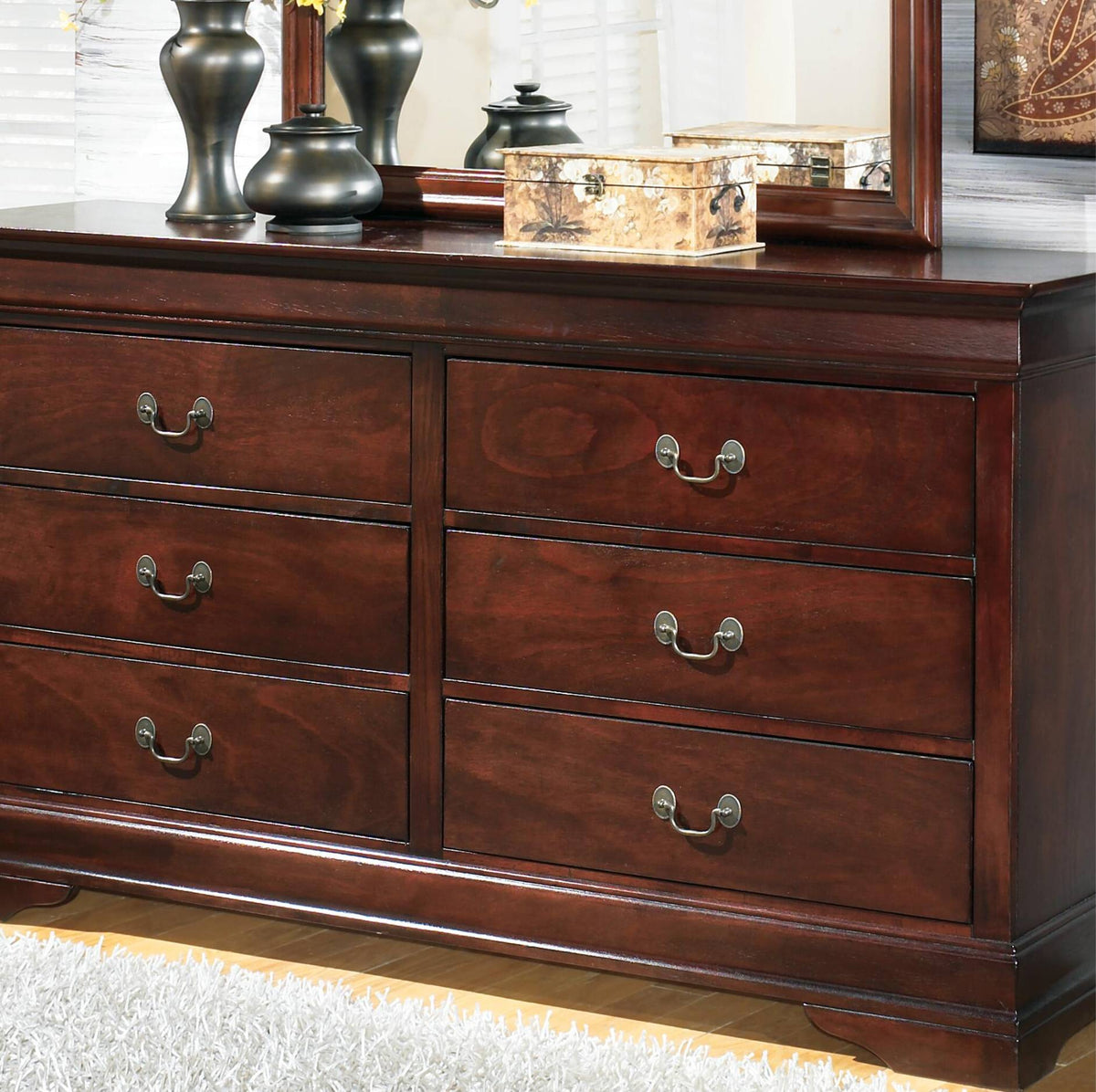 A dark reddish-brown wooden dresser with six drawers and silver metal handles, shown in a styled room setting with a mirror, decorative vases, and a patterned box on top.