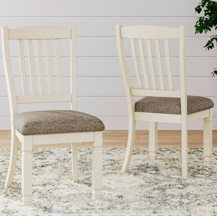 Two cream dining chairs with upholstered gray-brown seat cushions, shown on a shag rug against a white paneled wall.