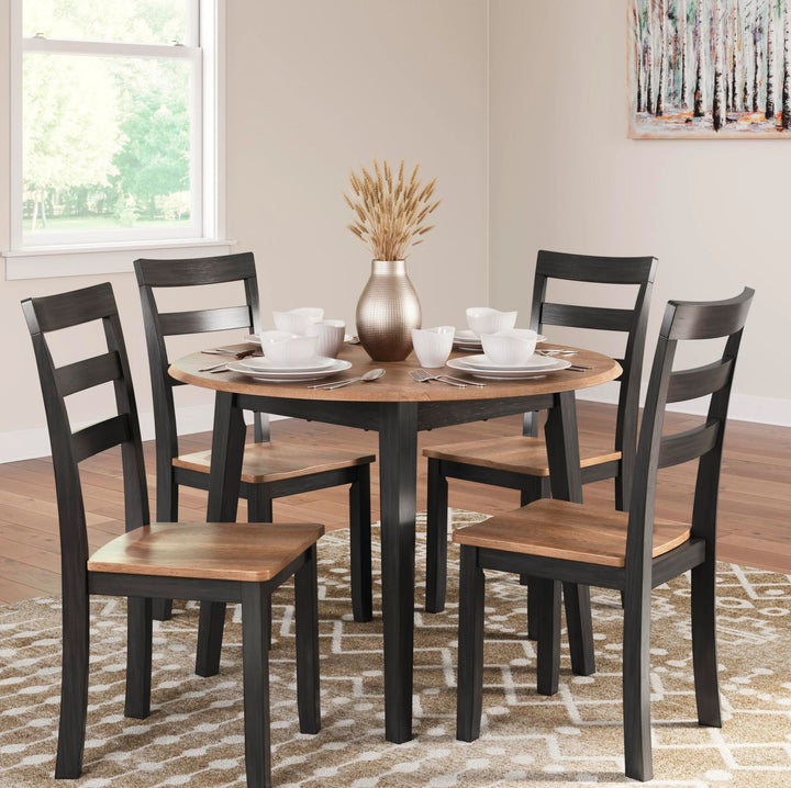 A 5-piece round dining table set with four black ladder-back chairs featuring light brown wooden seats, shown in a bright dining room setting with a window, patterned rug, and tableware.