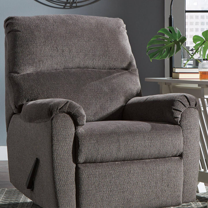 A plush upholstered recliner chair in dark taupe-brown textured fabric, shown in a modern living room setting with a side table, plant, and window in the background.