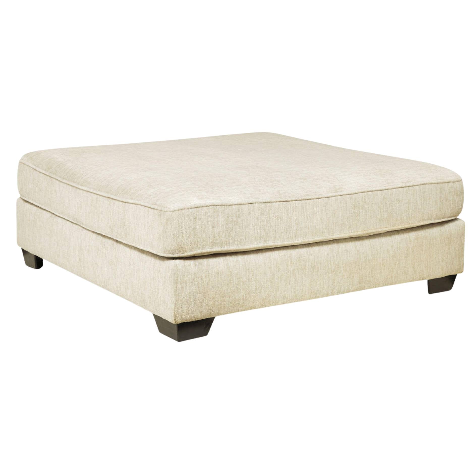 A square upholstered ottoman in a light beige textured fabric, shown from a three-quarter angle on a plain white background.