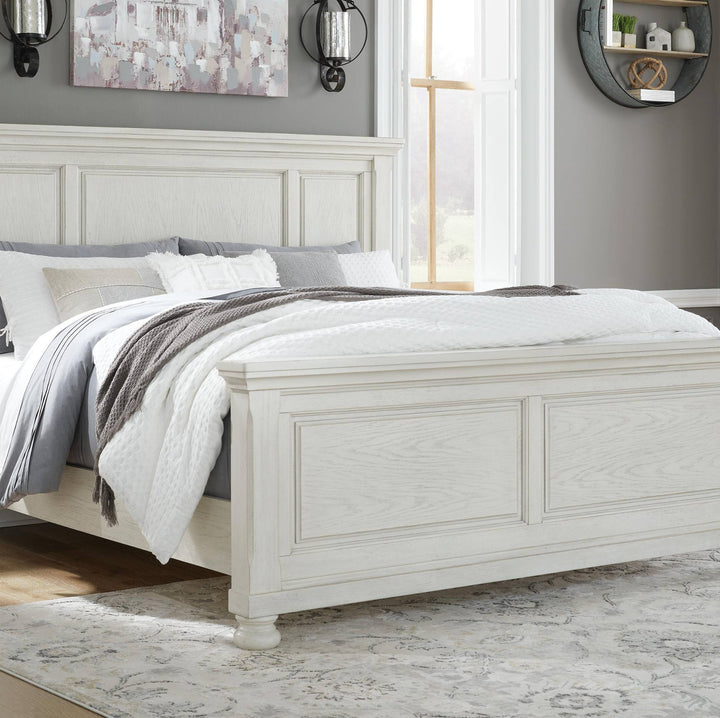 A white wooden bed frame with a paneled headboard and footboard, styled with white and gray bedding, a gray throw blanket, and set in a bedroom with a gray wall, window, and patterned rug.