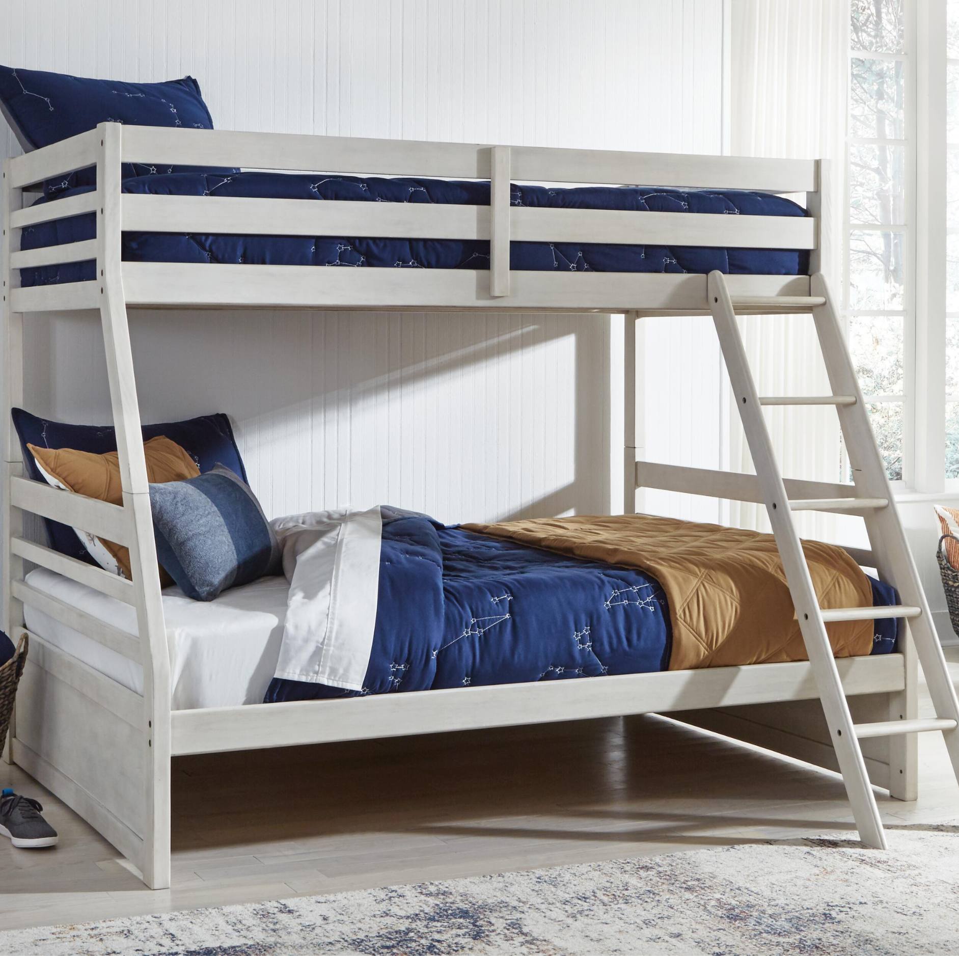 White wooden bunk bed frame with a ladder, styled with navy blue bedding, tan and blue pillows, in a bright bedroom setting.