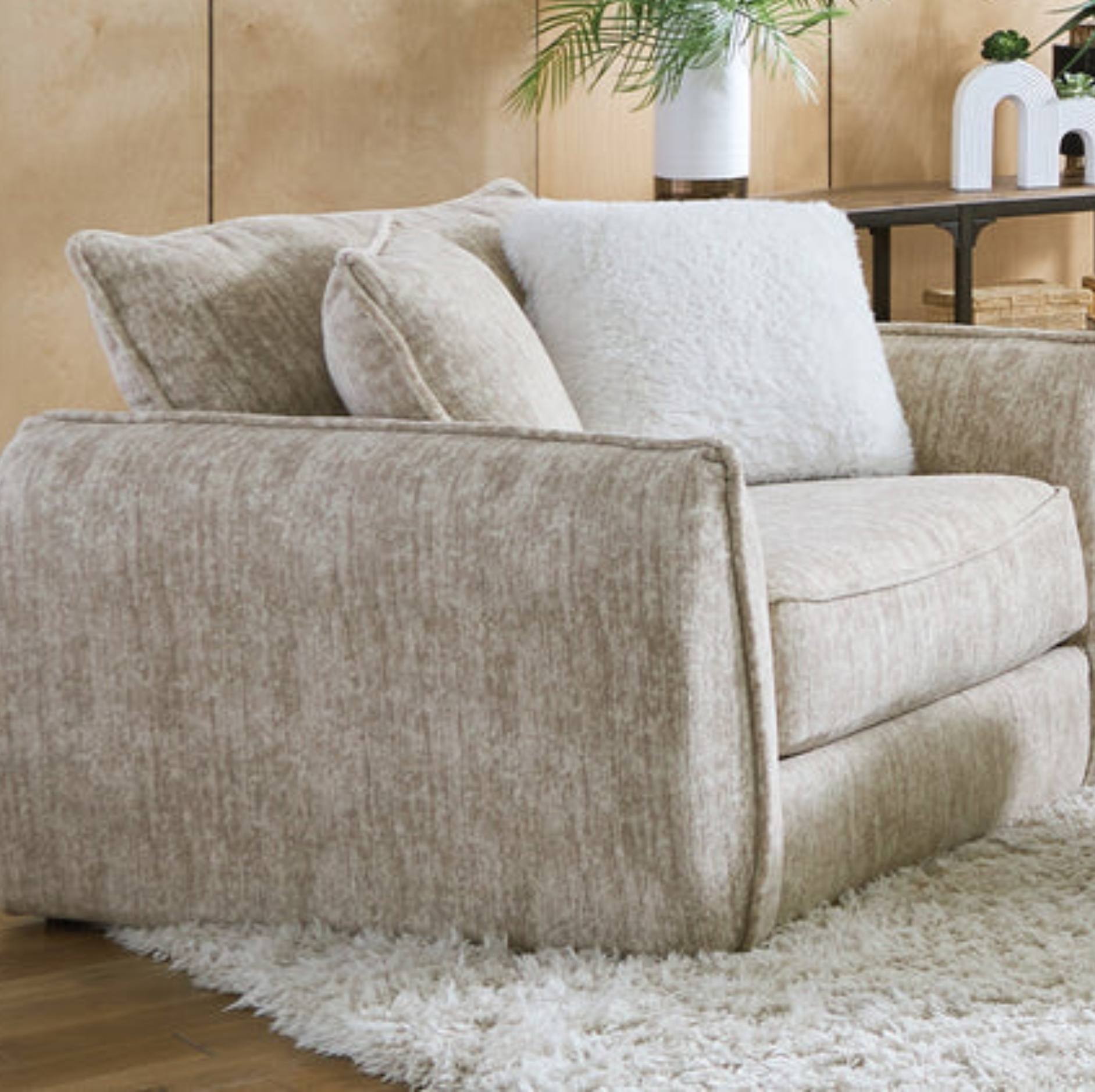 A beige upholstered armchair with textured fabric, shown in a styled living room setting on a white shag rug with a wooden floor and neutral wall background.