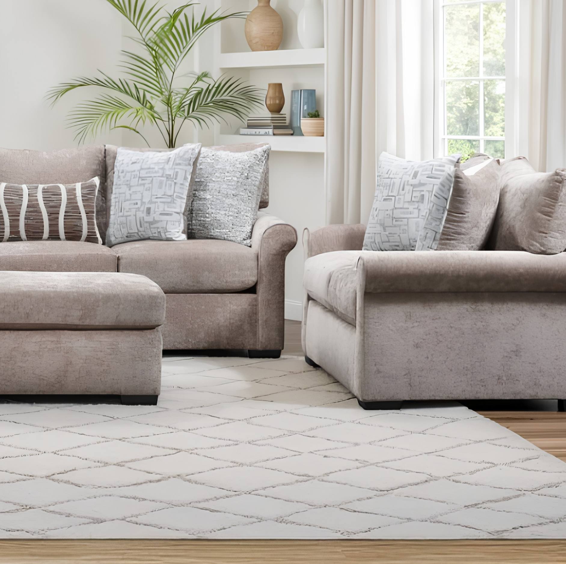 A coordinated living room furniture set featuring a taupe upholstered loveseat, matching ottoman, and a light beige armchair with patterned throw pillows, arranged on a white geometric area rug in a bright, modern living room.