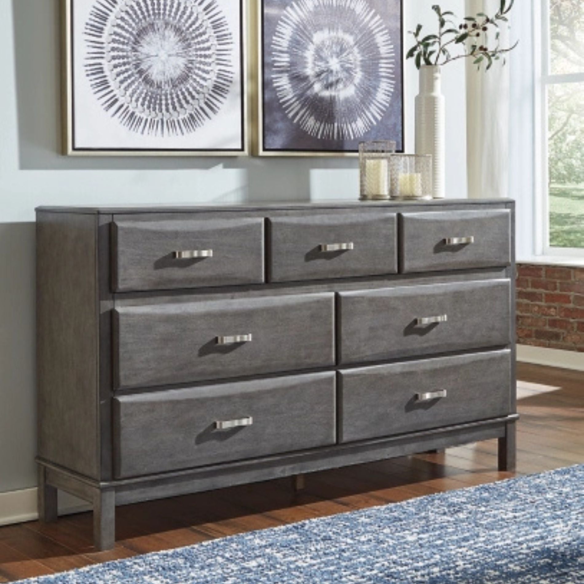 Gray dresser with multiple drawers in a room with artwork on the wall and a window.