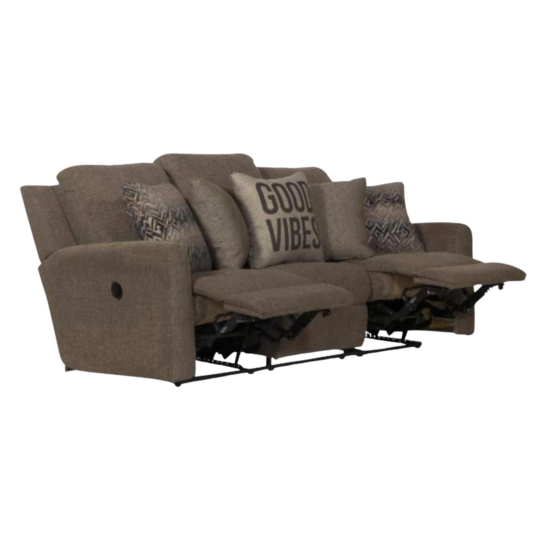 A three-seat recliner sofa in textured taupe-brown fabric, shown with two cushions extended. The sofa is styled with several throw pillows, including one that reads 'GOOD VIBES'.