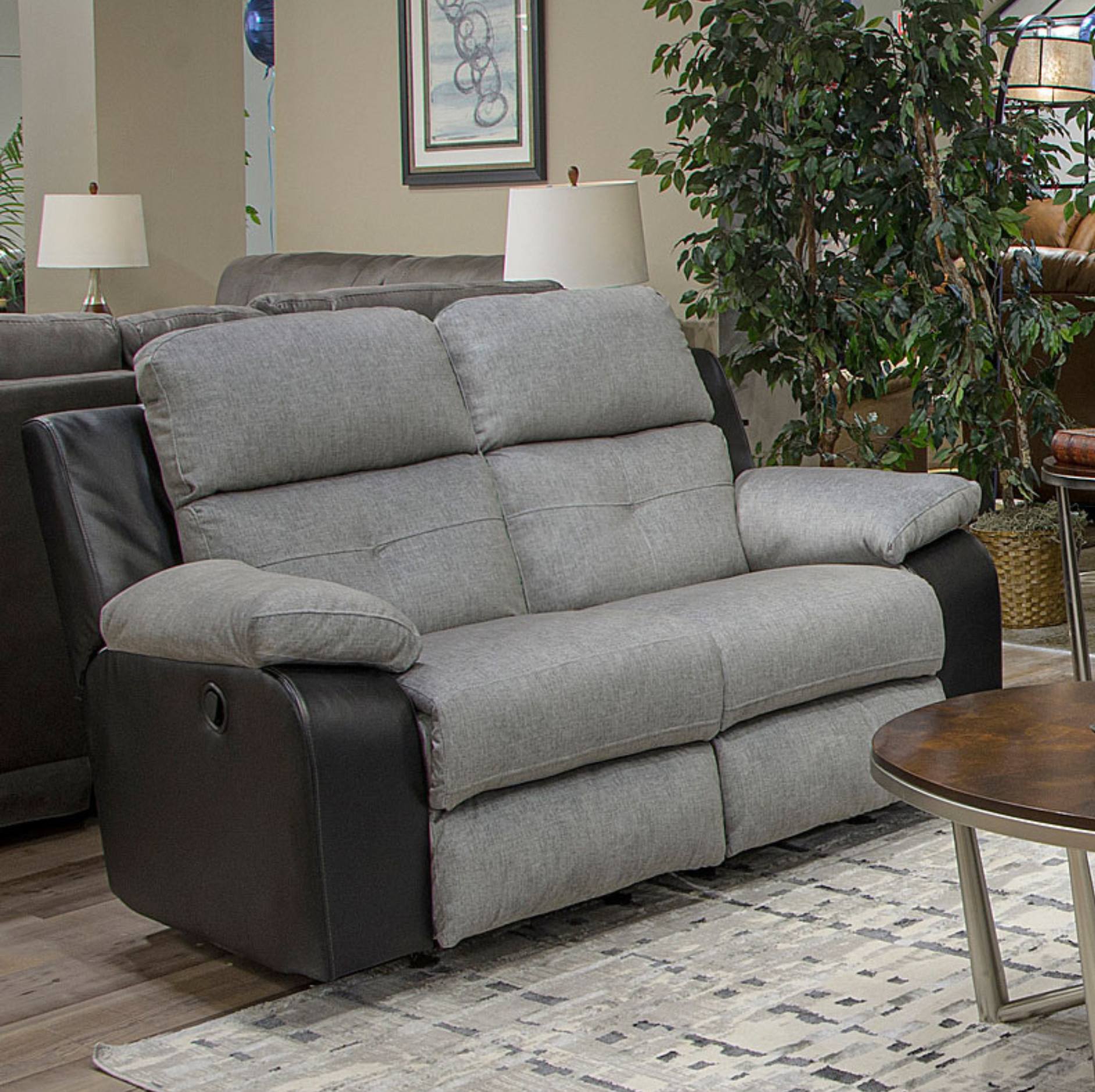 A two-seater power reclining loveseat sofa with light gray tufted fabric cushions and dark brown leather side panels, shown in a living room setting.