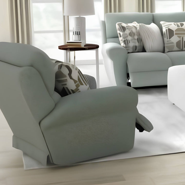 A light sage green recliner chair in a bright, modern living room setting, shown with a matching patterned throw pillow and a matching light green sofa in the background.