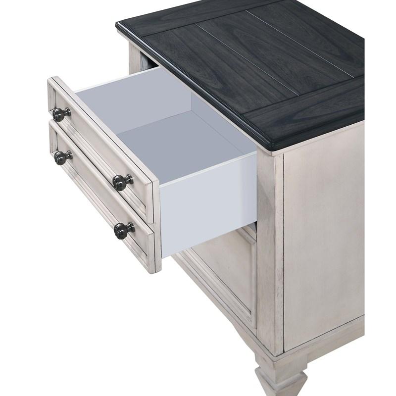 A close-up view of a light cream-colored wooden nightstand with a contrasting dark wood top. The top drawer is pulled open to reveal a clean, spacious interior, highlighting the dark metal knob hardware.