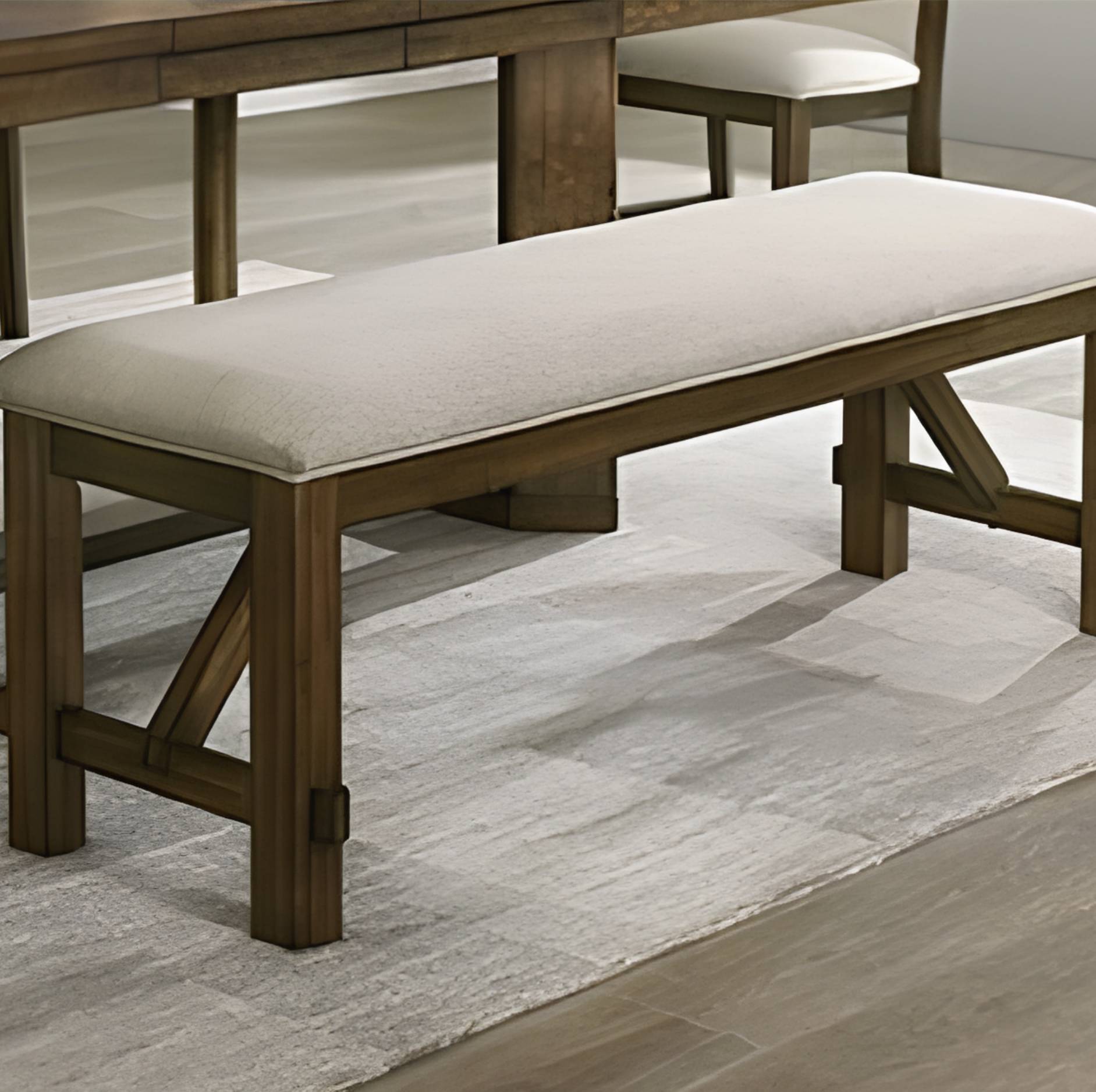 A wooden dining bench with a thick cream upholstered seat cushion, shown in a dining room setting on a light rug.