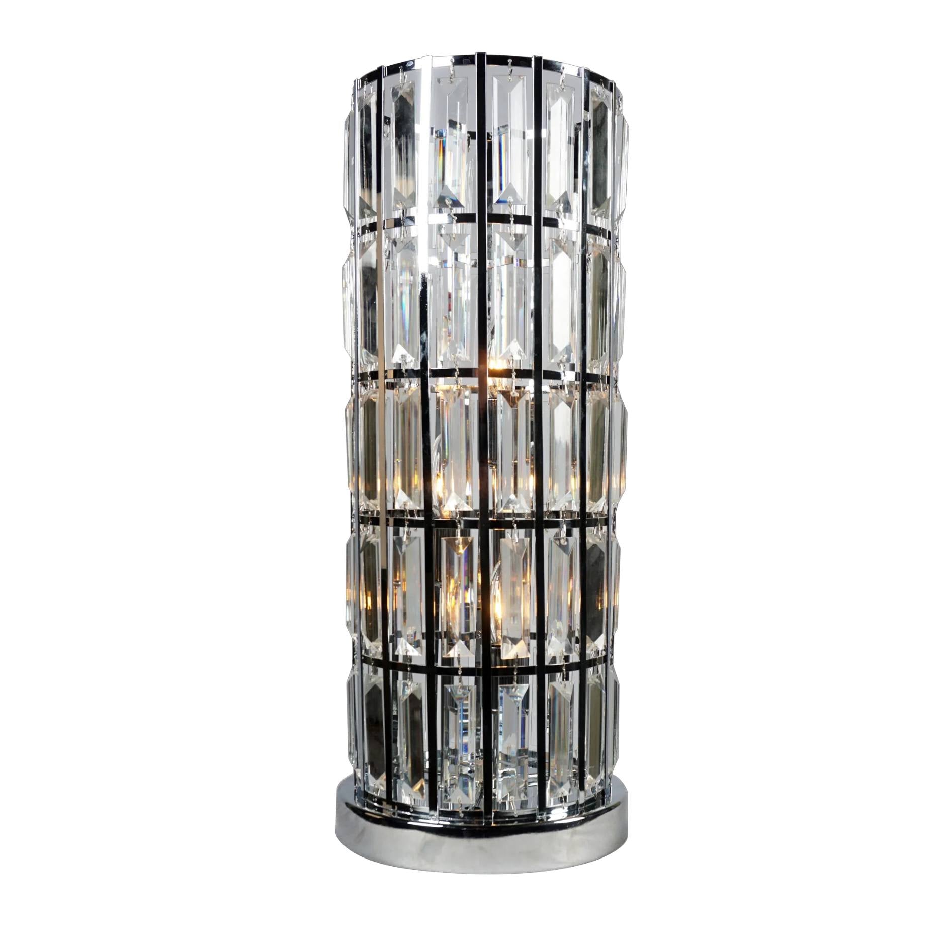 A modern cylindrical table lamp with a polished chrome base and frame, featuring multiple stacked clear glass prisms that glow with warm light, set against a plain white background.