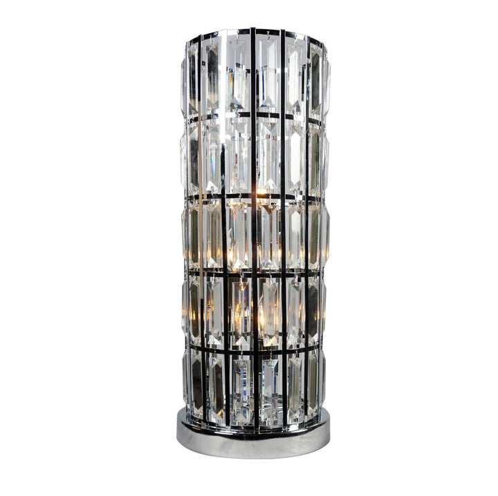 A modern cylindrical table lamp with a polished chrome base and frame, featuring multiple stacked clear glass prisms that glow with warm light, set against a plain white background.