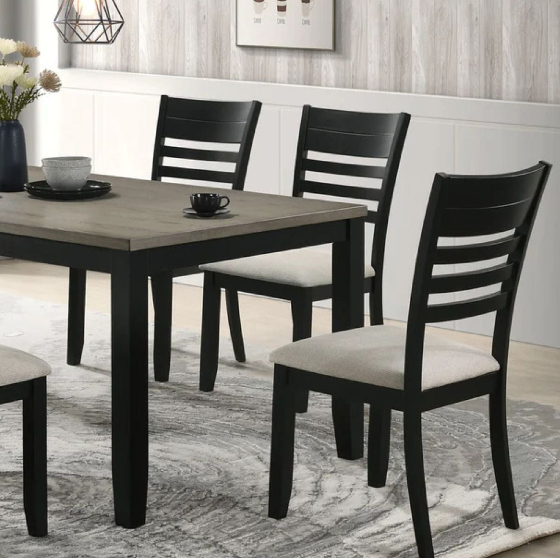 A 5-piece dining set featuring a rectangular table with a gray wood-grain top and black frame, accompanied by four matching chairs with black frames and light beige upholstered seats, set on a gray patterned rug in a dining room.