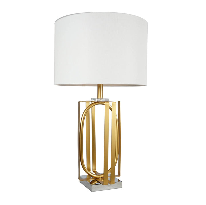 A modern table lamp featuring a white drum shade and a polished gold-finished metal base with vertical bars and an oval frame, set against a plain white background.