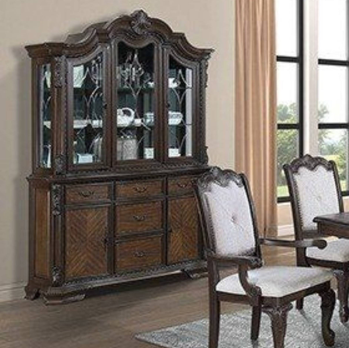 A dark brown carved wooden hutch with glass-front upper cabinets and lower drawers, shown in a dining room setting next to matching chairs and a table.