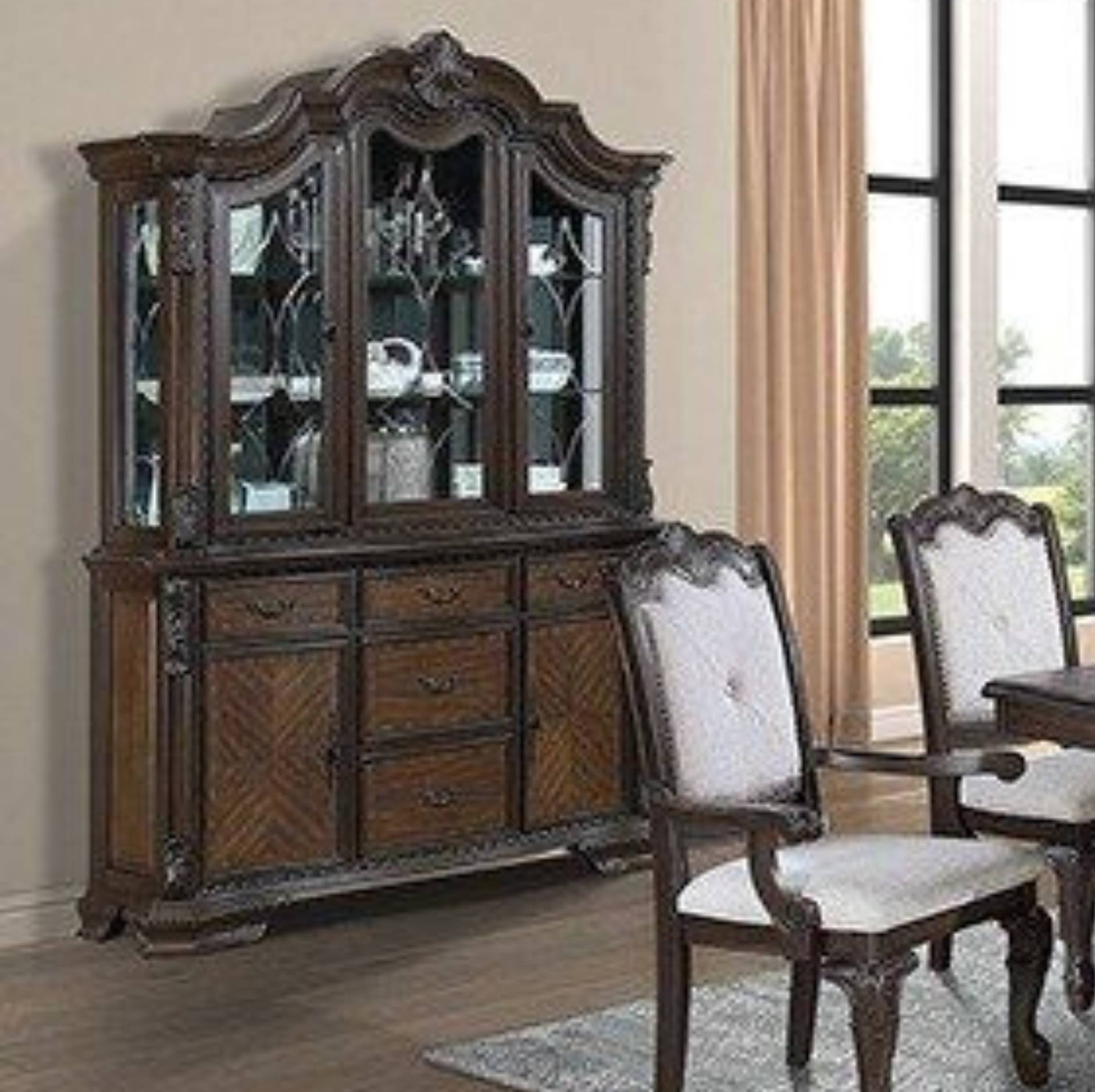 A dark brown carved wooden hutch with glass-front upper cabinets and lower drawers, shown in a dining room setting next to matching chairs and a table.