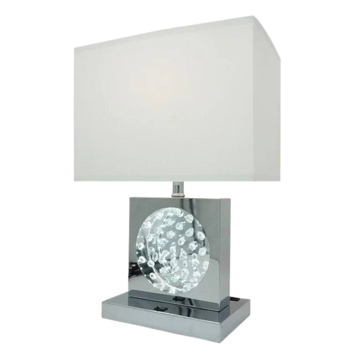 A modern table lamp with a rectangular white fabric shade, a polished chrome square base, and a clear faceted crystal sphere in the center.