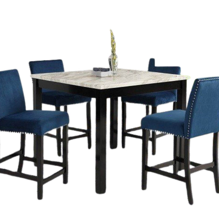 A 5-piece counter height dining set featuring a square table with a light marble-patterned top and black frame, surrounded by four blue velvet barstools with nailhead trim.
