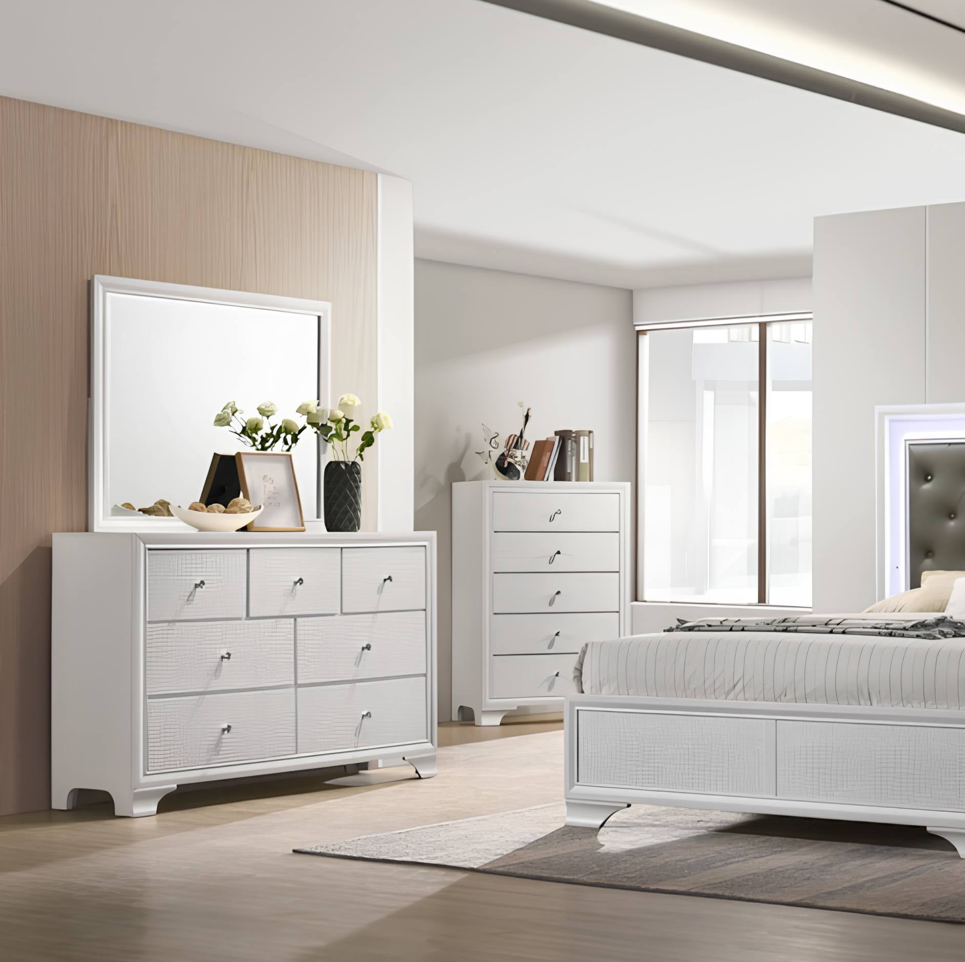 A modern bedroom furniture set featuring a white six-drawer dresser with a matching rectangular mirror, a white three-drawer chest, and a white bed frame, arranged in a bright, contemporary bedroom with light wood flooring and beige walls.