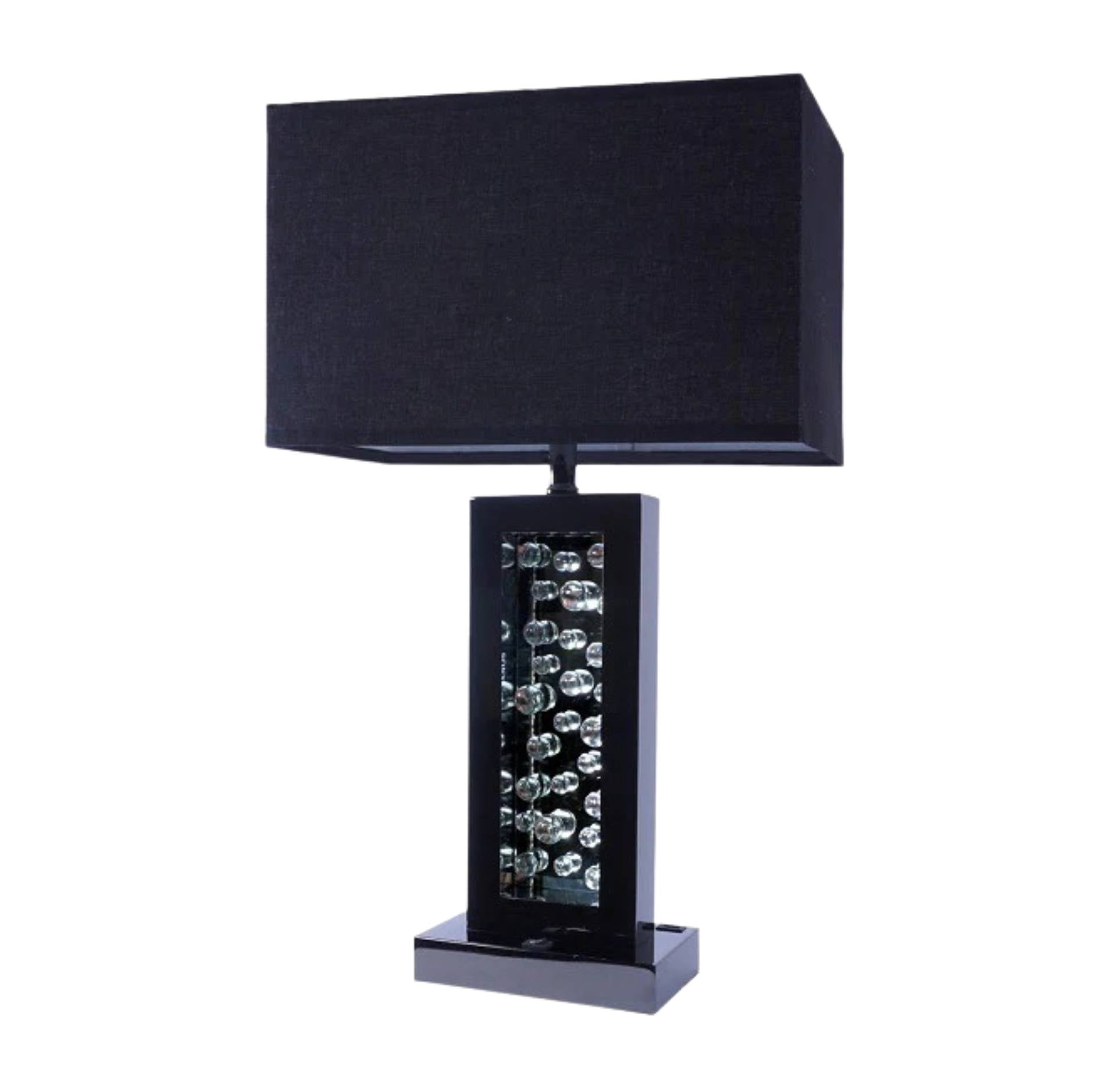 A modern table lamp with a black fabric drum shade, a glossy black rectangular base, and a central column of clear faceted crystal prisms, shown on a plain white background.