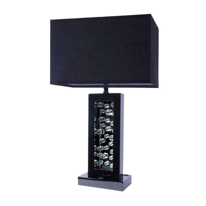 A modern table lamp with a black fabric drum shade, a glossy black rectangular base, and a central column of clear faceted crystal prisms, shown on a plain white background.