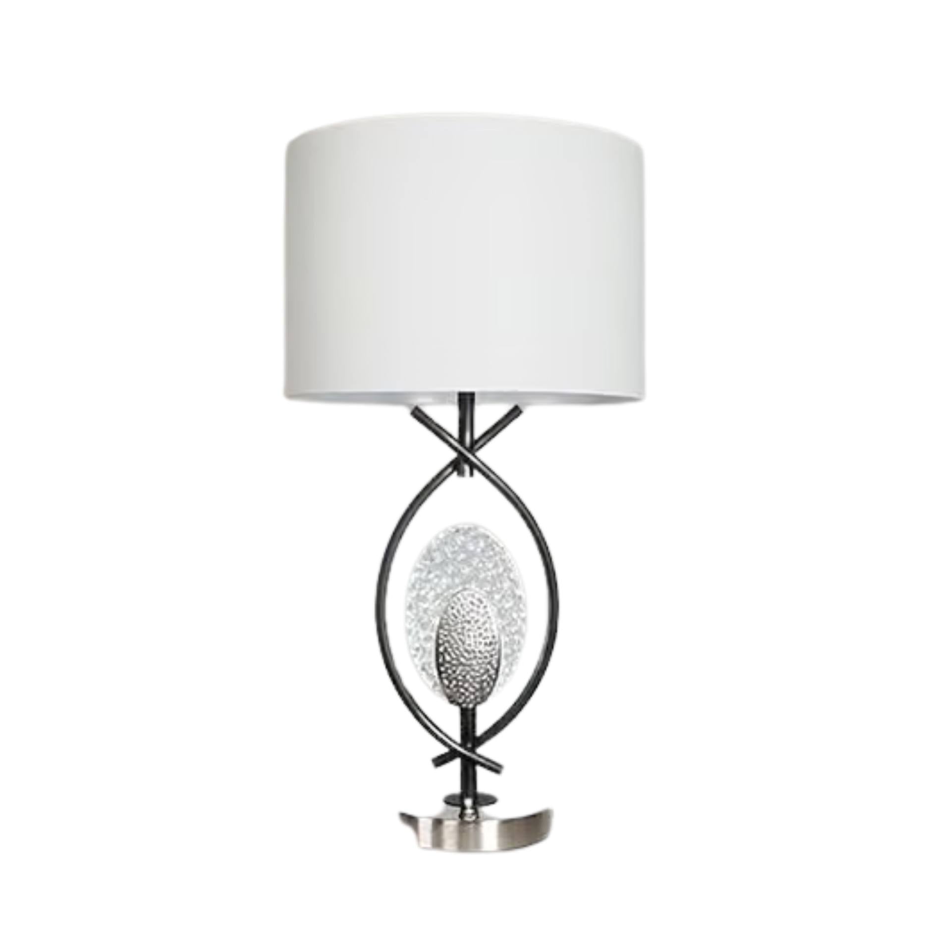 A modern table lamp with a white drum shade, a black metal frame, a textured silver oval center, and a polished silver base, shown against a plain white background.
