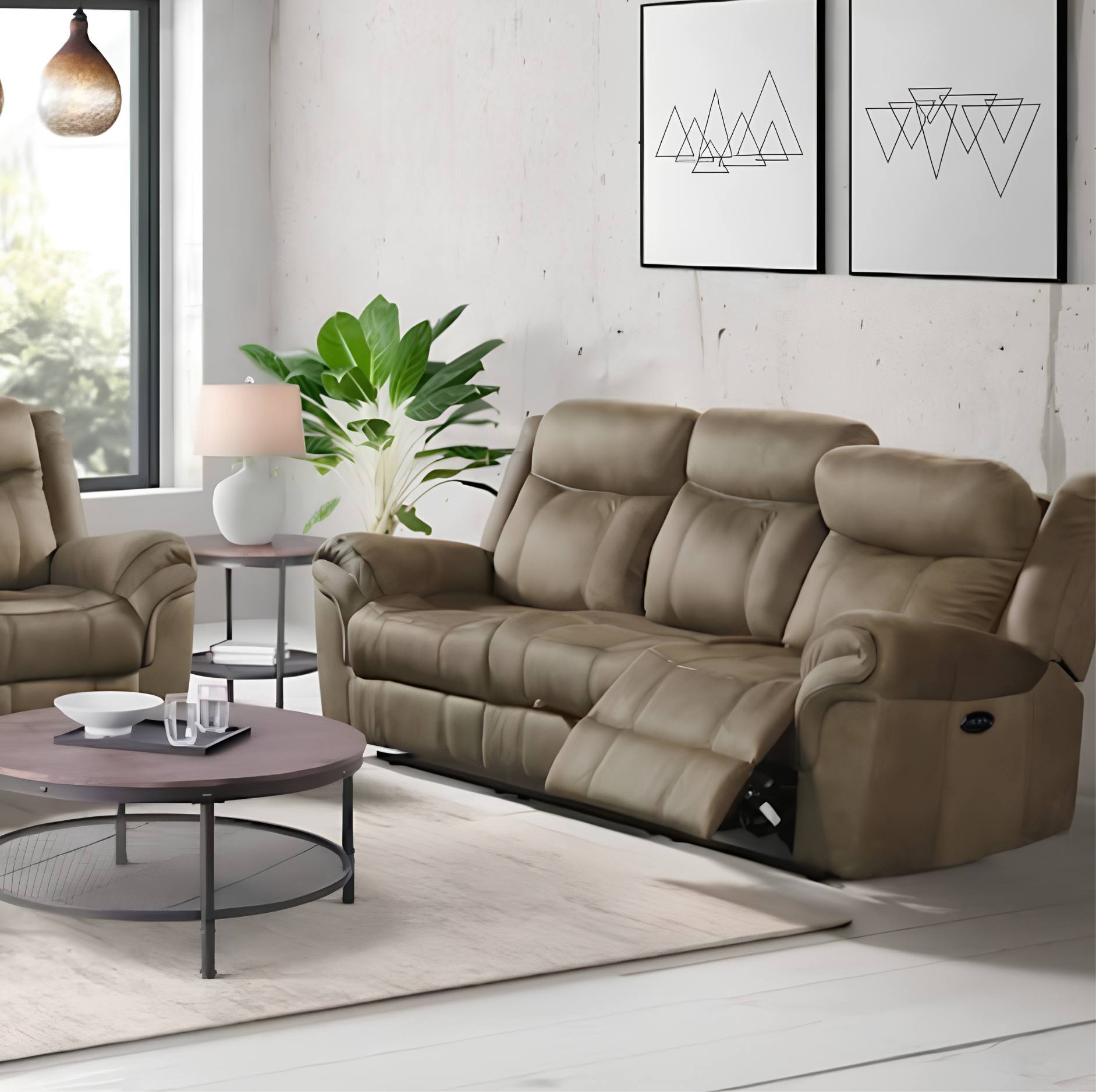 A taupe-brown reclining three-seater sofa in a modern living room setting, shown with its front recliner cushion extended. The sofa is styled in a bright, contemporary room with a matching armchair, a round coffee table, a potted plant, and minimalist wall art.