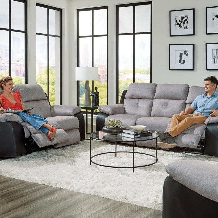 Living room with gray sofa set and people sitting on it, large windows in the background