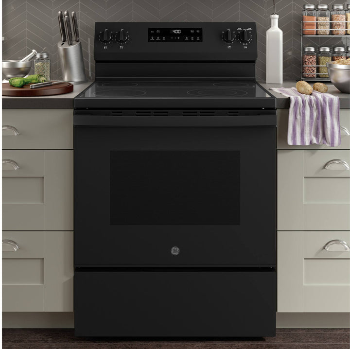 A black GE freestanding electric range with a glass cooktop and oven door, set in a kitchen with light gray cabinets and a gray herringbone backsplash.