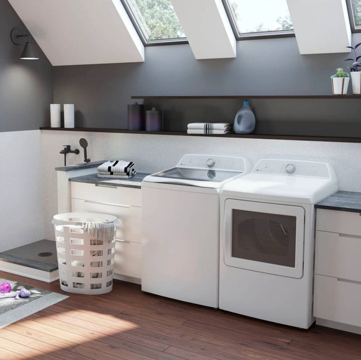 A white top-loading washer and matching white dryer installed in a modern laundry room with gray walls, wood floors, built-in cabinets, and skylights.