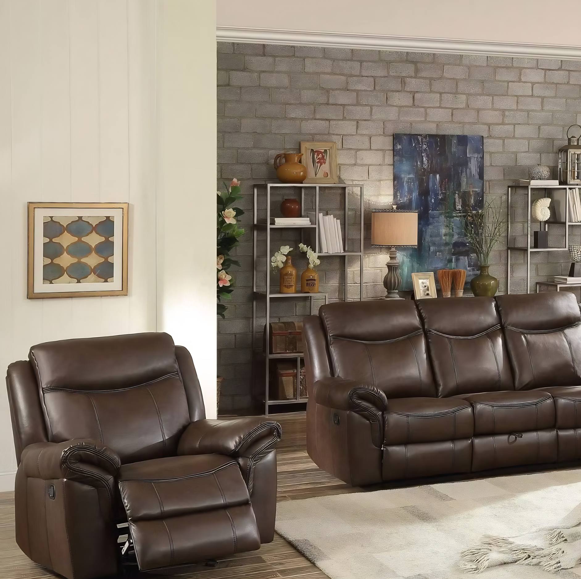 A brown leather recliner chair and matching three-seat sofa arranged in a styled living room with a brick accent wall, shelving, artwork, and a light rug.
