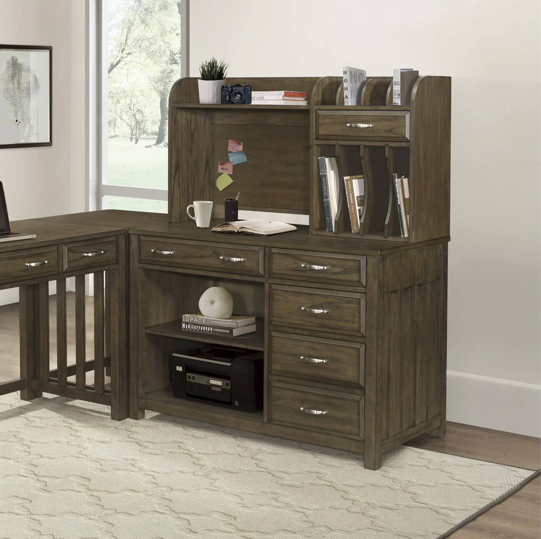 A rustic brown L-shaped corner desk set with a hutch, shown in a home office environment with a window, rug, and wall art.