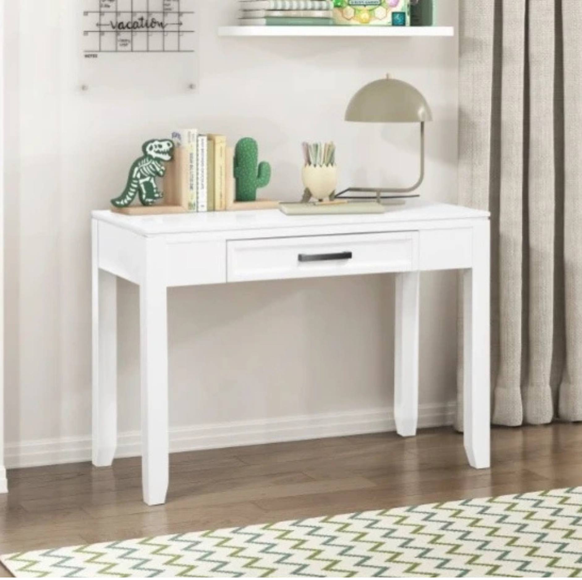 A white wooden writing desk with a single drawer and black metal handle, styled in a home office setting with a lamp, books, and a dinosaur figurine on top.