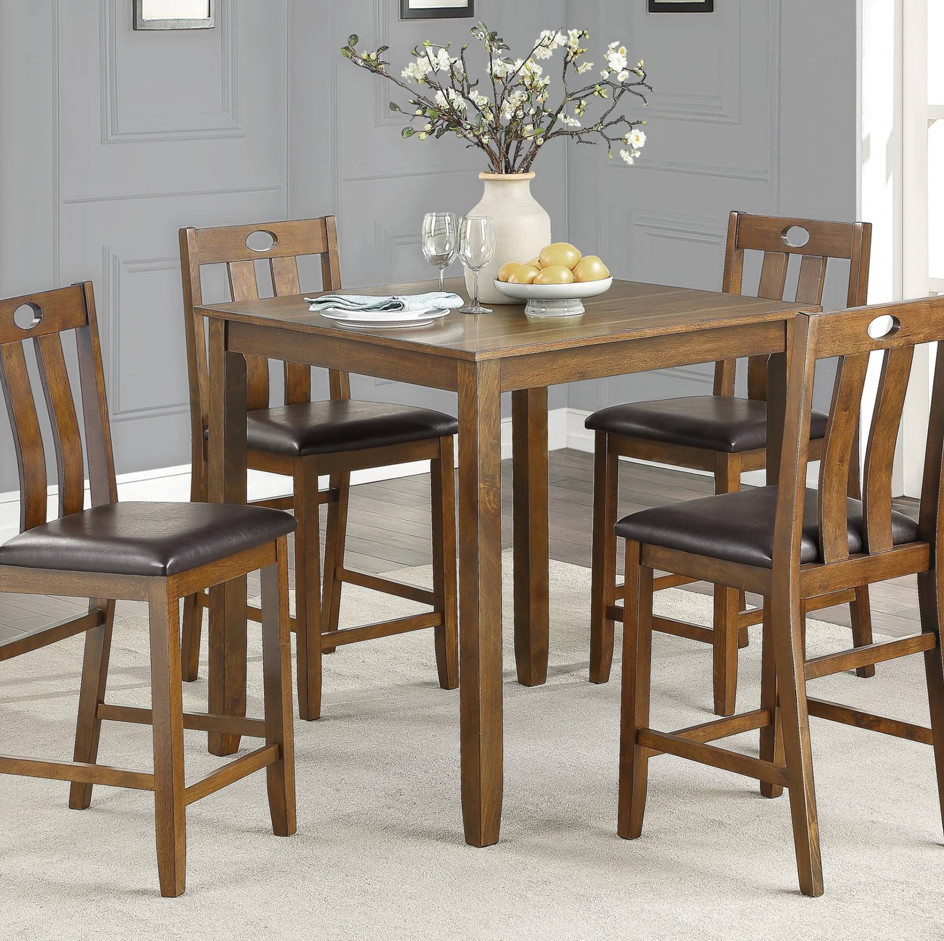 A 5-piece wooden counter height dining set including a square table and four matching stools with dark brown upholstered seats, shown in a dining room setting.