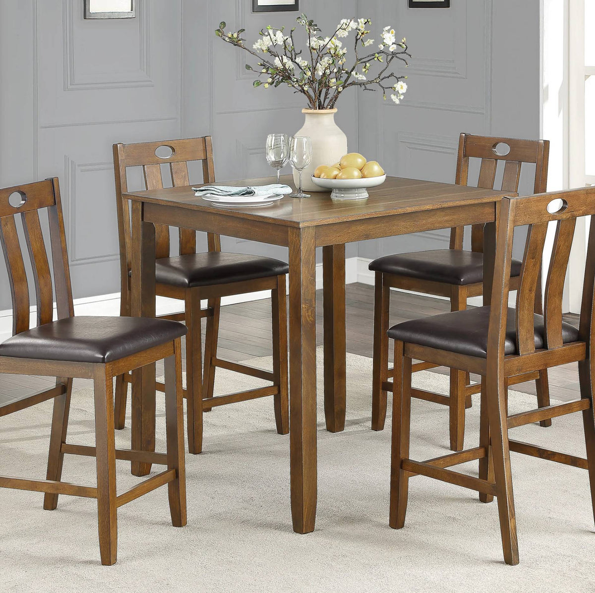 A 5-piece wooden counter height dining set including a square table and four matching stools with dark brown upholstered seats, shown in a dining room setting.