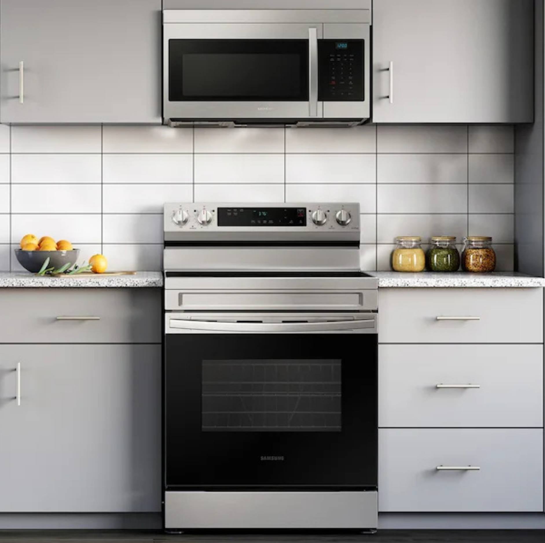 A stainless steel freestanding electric range with a black glass oven door, set in a modern kitchen with light gray cabinets, a white subway tile backsplash, and a matching stainless steel microwave mounted above.