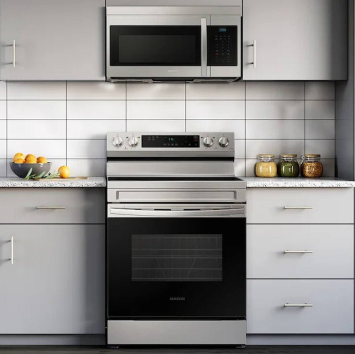 A stainless steel freestanding electric range with a black glass oven door, set in a modern kitchen with light gray cabinets, a white subway tile backsplash, and a matching stainless steel microwave mounted above.