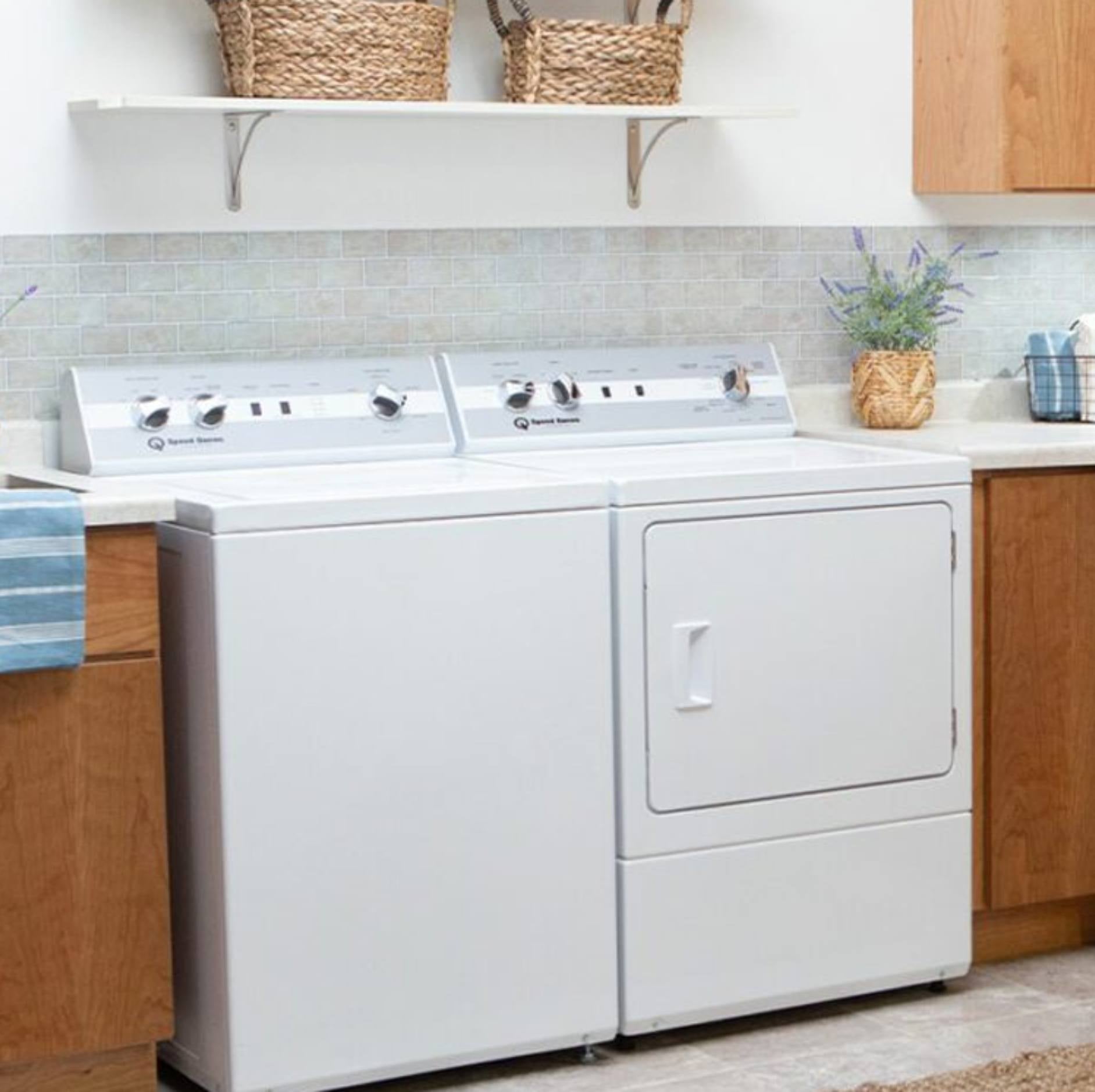 A white GE brand dryer and matching washer side-by-side in a bright, modern laundry room with light wood cabinets, a tiled backsplash, and a blue striped towel.